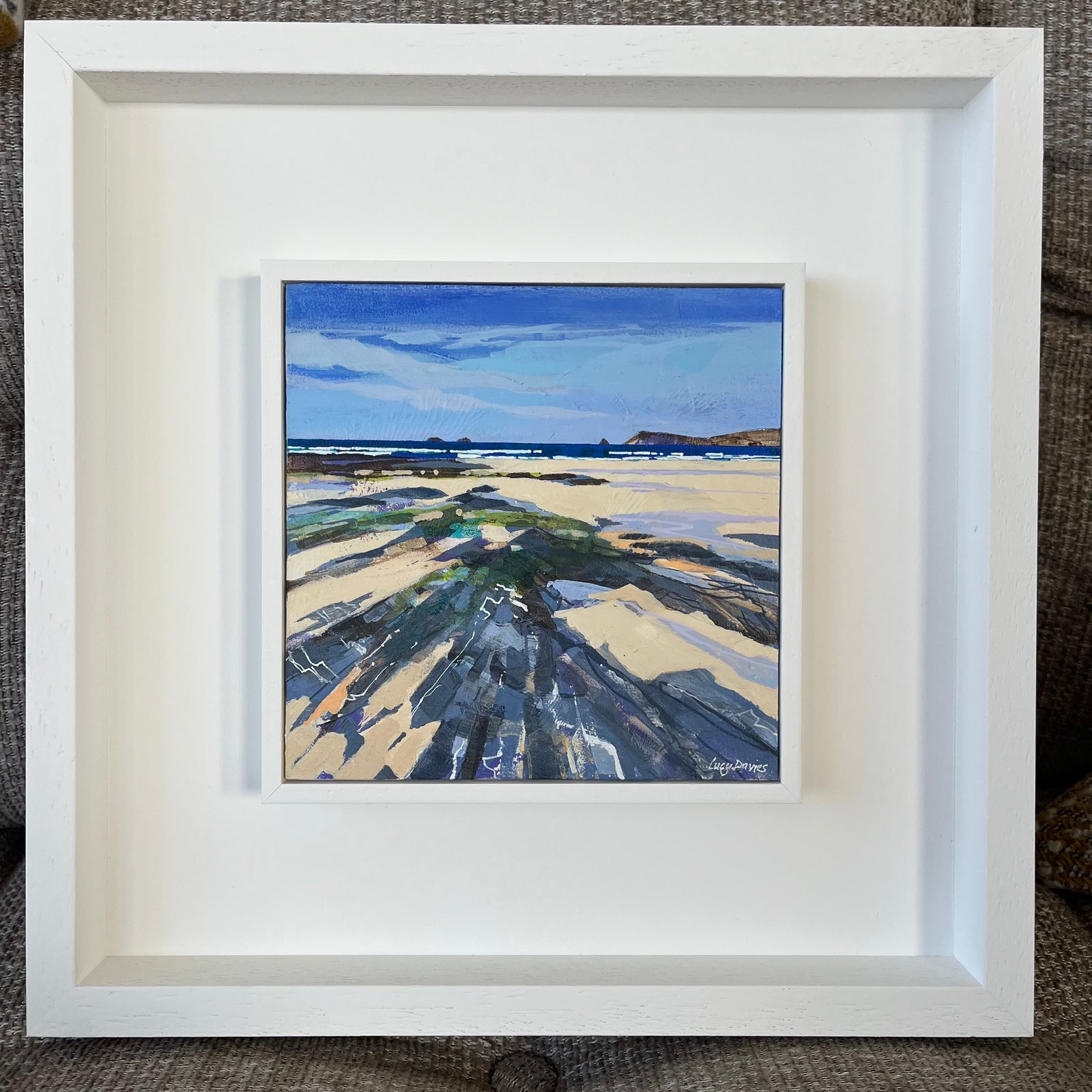 Framed painting of a coastal landscape with a white frame.